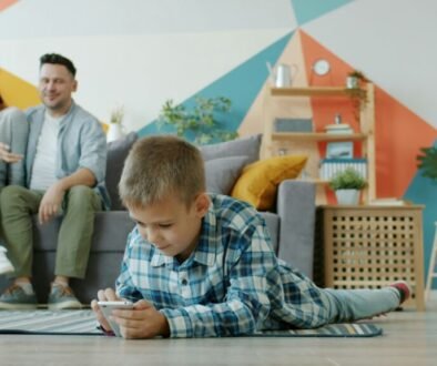 A child using a smartphone while parents sit nearby, used as an editorial illustration for a family screen-time conversation.