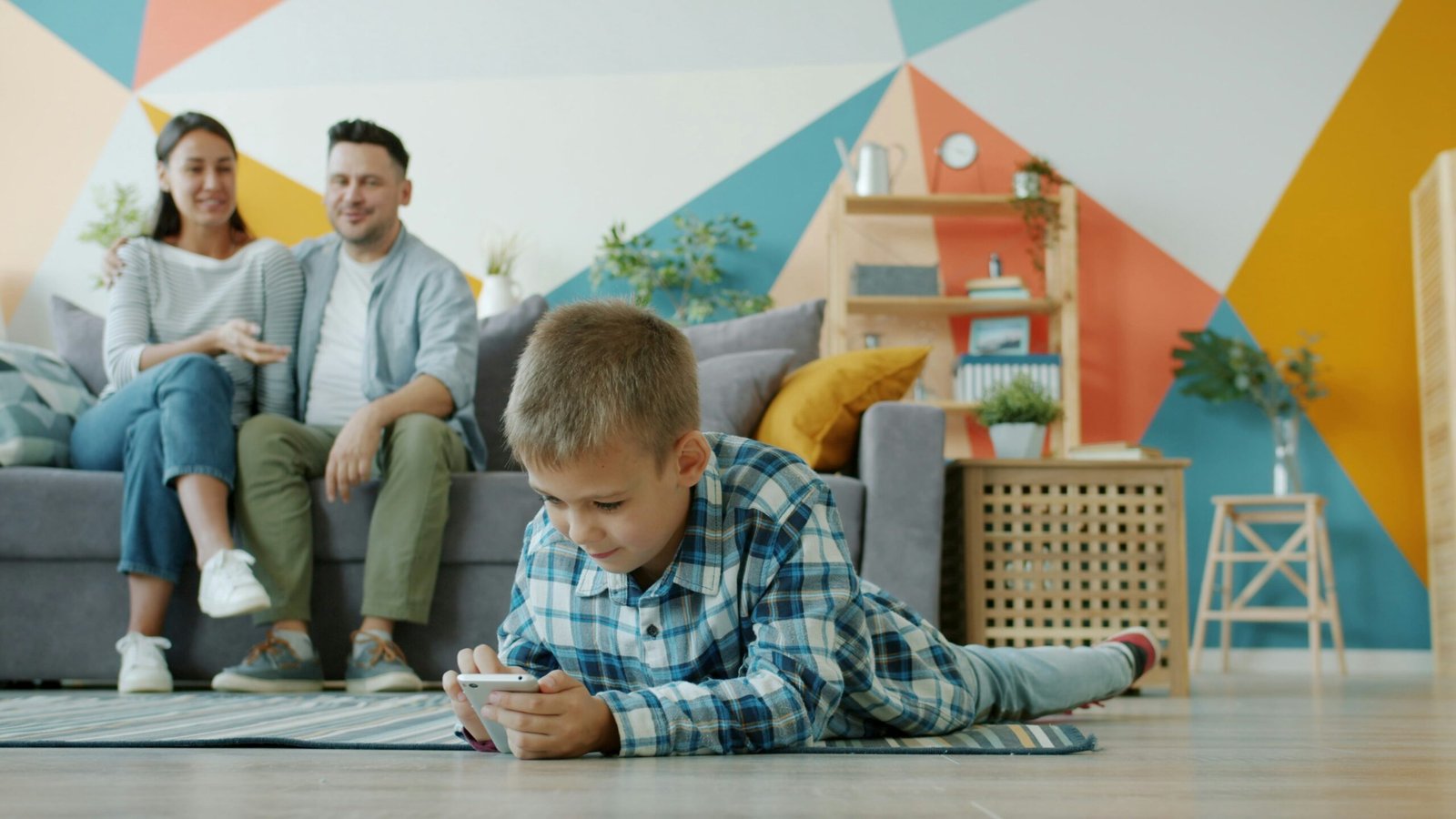 A child using a smartphone while parents sit nearby, used as an editorial illustration for a family screen-time conversation.