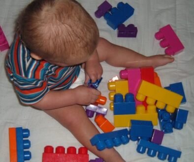 A young child sits on the floor and plays with large building blocks independently.