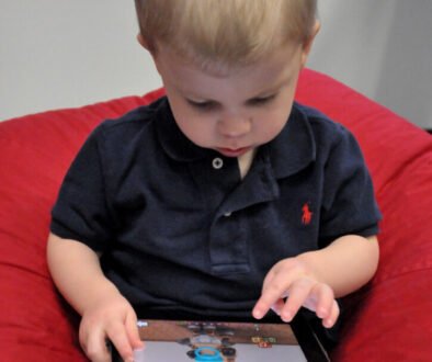 Young child using a tablet while an adult is nearby