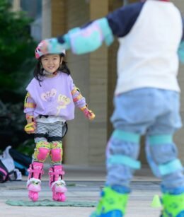 Two children rollerblading outdoors while wearing protective sports gear.