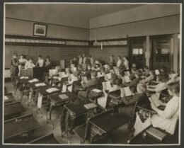 Black-and-white historical photograph of children reading in a classroom.
