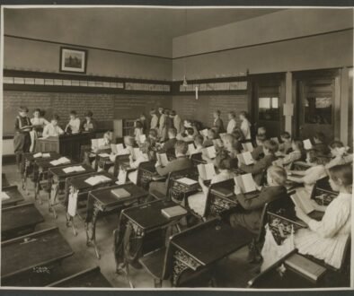 Black-and-white historical photograph of children reading in a classroom.