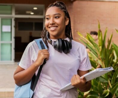 Student carrying a backpack and books outdoors.