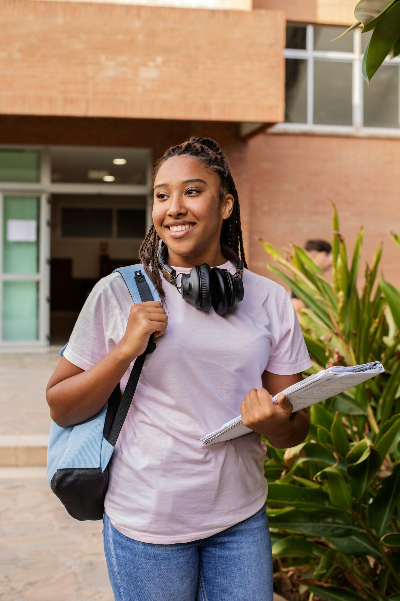 Student carrying a backpack and books outdoors.