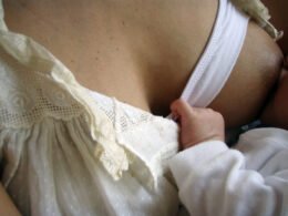 A mother breastfeeds a baby while wearing a nursing bra.