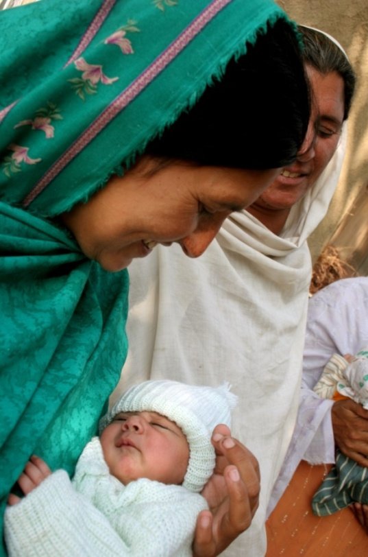 A mother gently holds her newborn baby close during a calm daytime moment.
