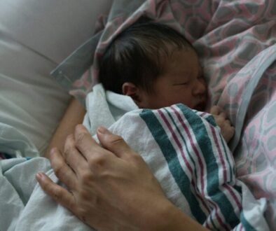 A newborn rests in a parent’s arms; editorial image for guidance about newborn grunts and straining during sleep.