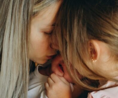 Two older sisters gently hold and look at their newborn sibling.