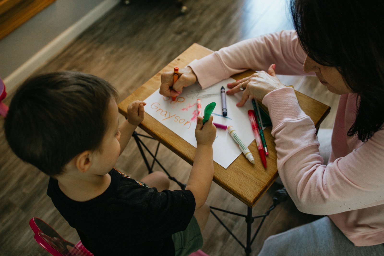 An adult and young child color together at a table during a calm shared activity.