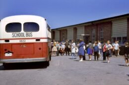 Children standing near a yellow school bus outside a school building