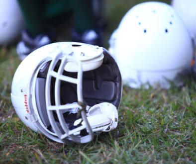 Sports helmets rest on a football field before a game; public-domain image used as an editorial illustration for helmet hygiene.