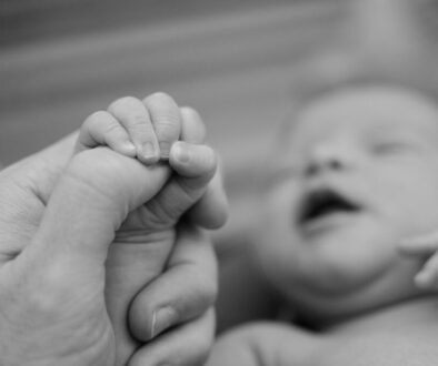 A newborn holds an adult finger, illustrating gentle newborn nail care.