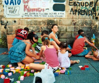 A caregiver sits with young children who are playing with building blocks at a child-care setting.