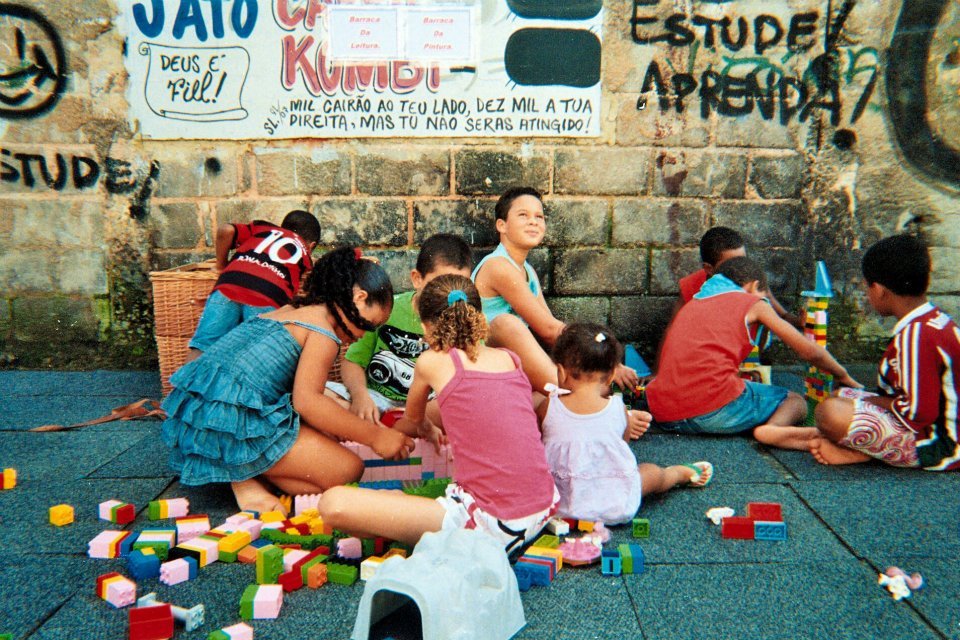 A caregiver sits with young children who are playing with building blocks at a child-care setting.