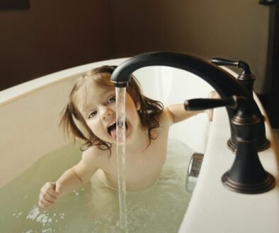 Toddler sitting in a bathtub near a faucet.