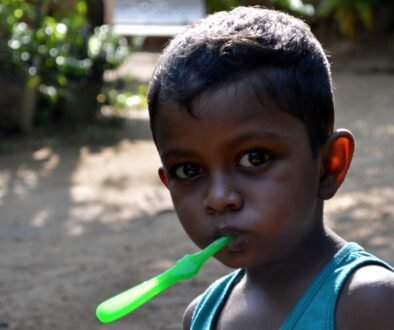 A young child brushes their teeth with a small toothbrush.